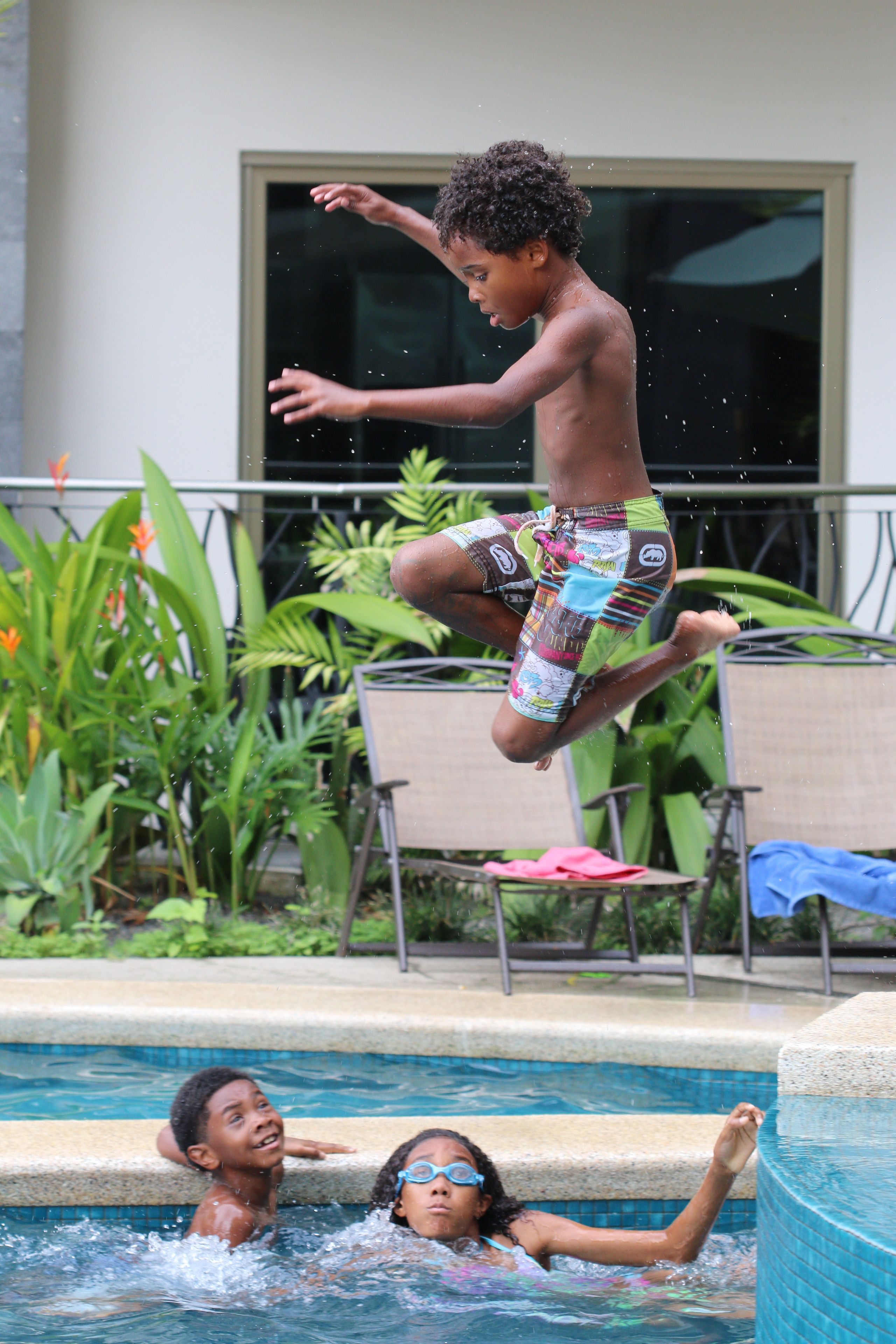 A child jumping into a swimming pool with another child in the water.