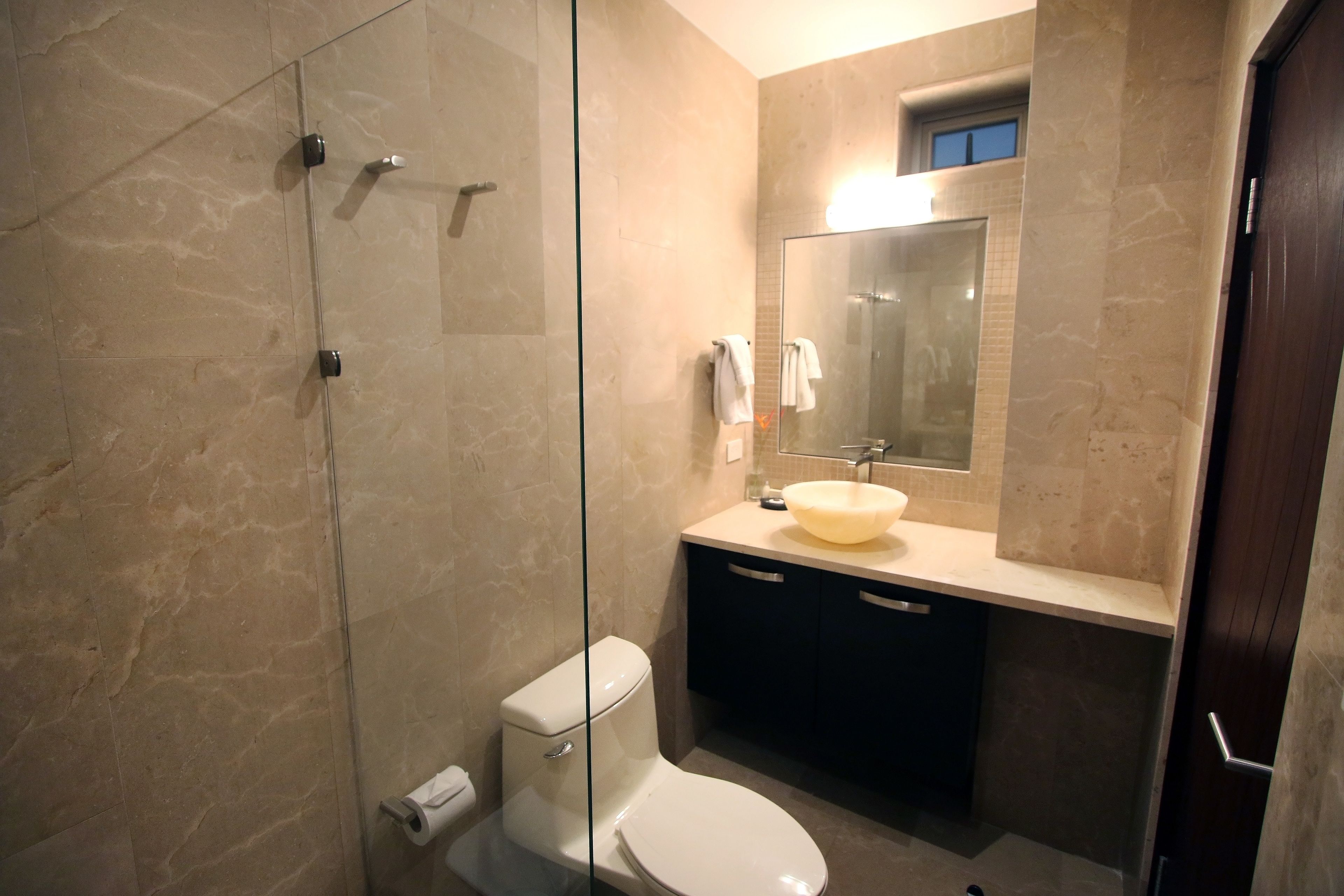 A modern bathroom with a glass shower enclosure, a white toilet, and a beige sink with a mirror above it.