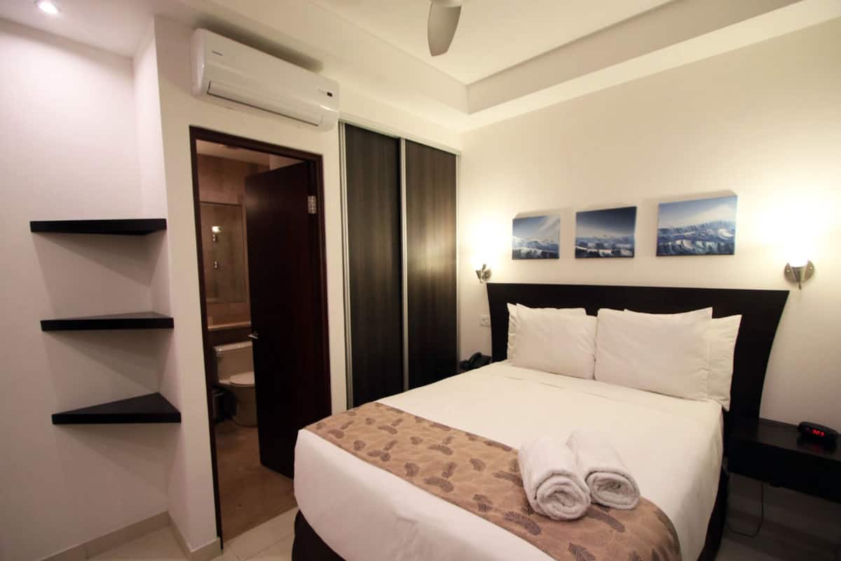 A hotel room with a bed, a wardrobe, a shelf, and a wall-mounted air conditioner.