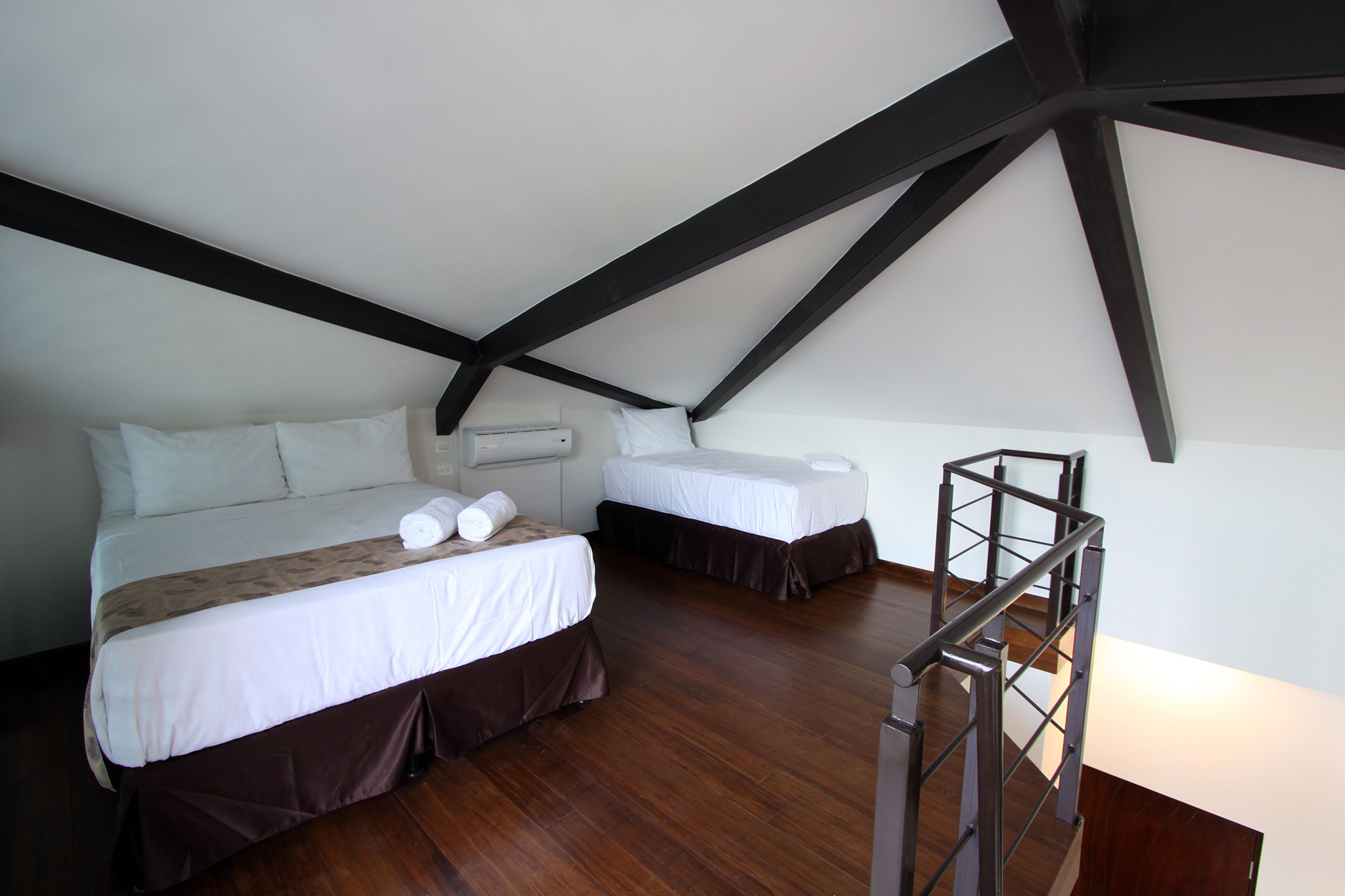A bedroom with two beds, a wooden floor, and a staircase.