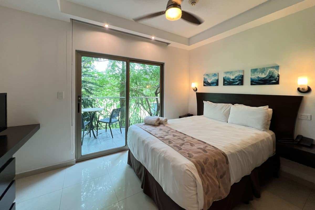 A bedroom with a bed, a ceiling fan, a nightstand, and a view of the outdoors through a sliding door.