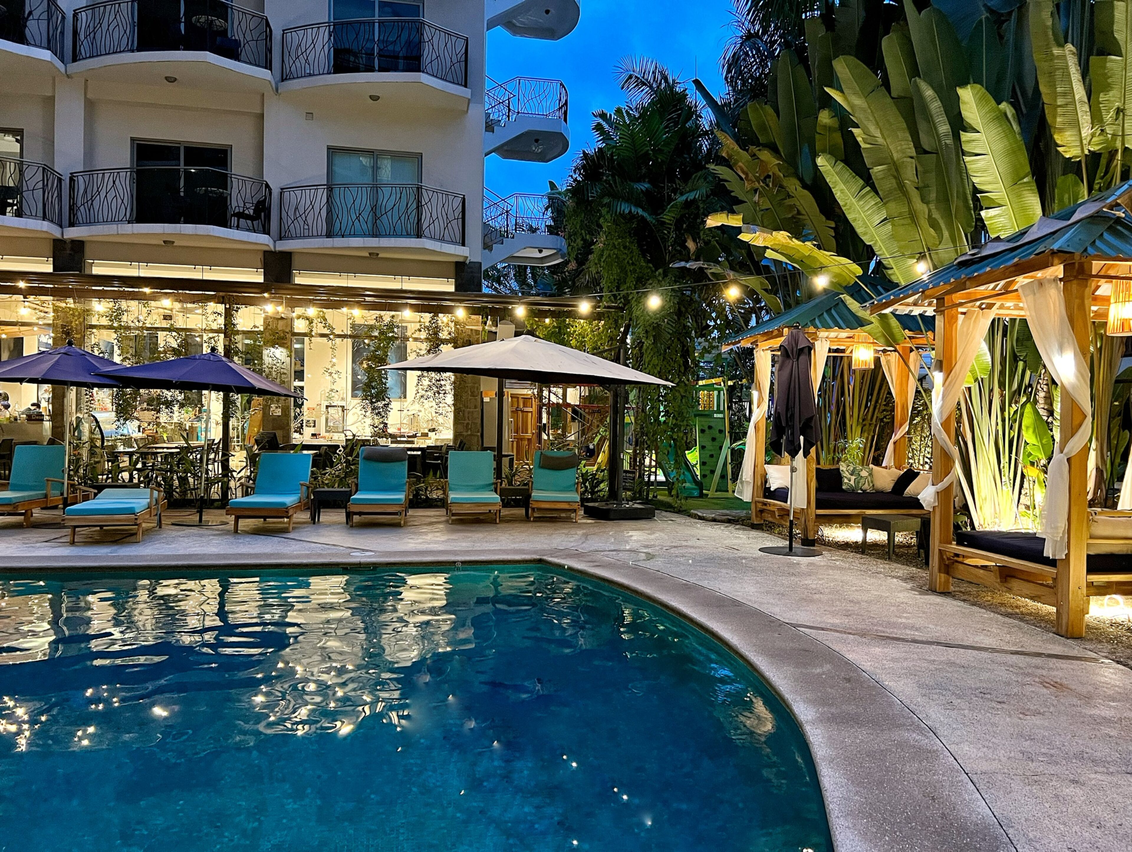 A pool area with lounge chairs and umbrellas, surrounded by a building with balconies and outdoor seating.
