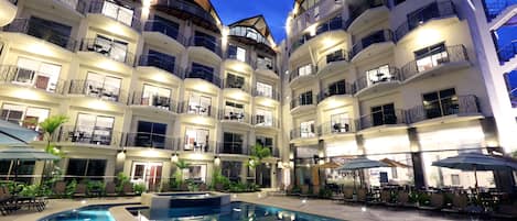 Un hotel de varios pisos con balcones, piscina y zonas de estar al aire libre.