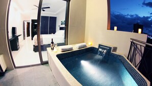 A modern hotel room with a private balcony, a large window, and a view of the city skyline at dusk.