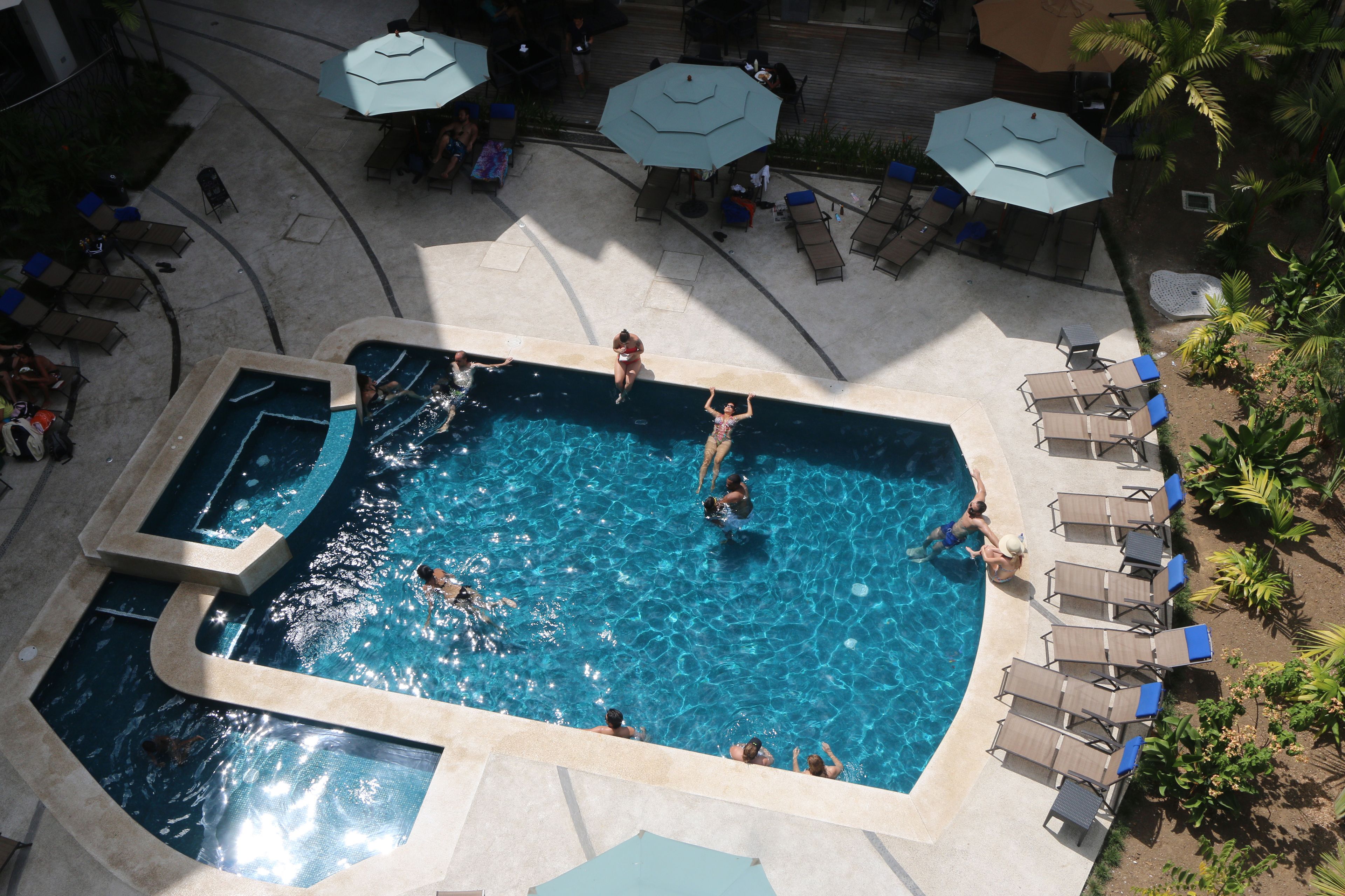 A large outdoor swimming pool with multiple sections, surrounded by lounge chairs and umbrellas.