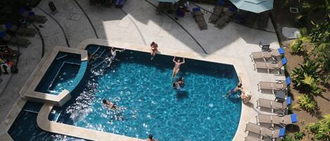 A large outdoor swimming pool with multiple sections, surrounded by lounge chairs and umbrellas.