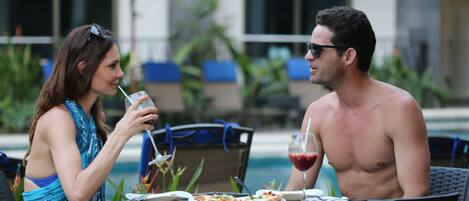 Two people dining outdoors at a table with a pool in the background.