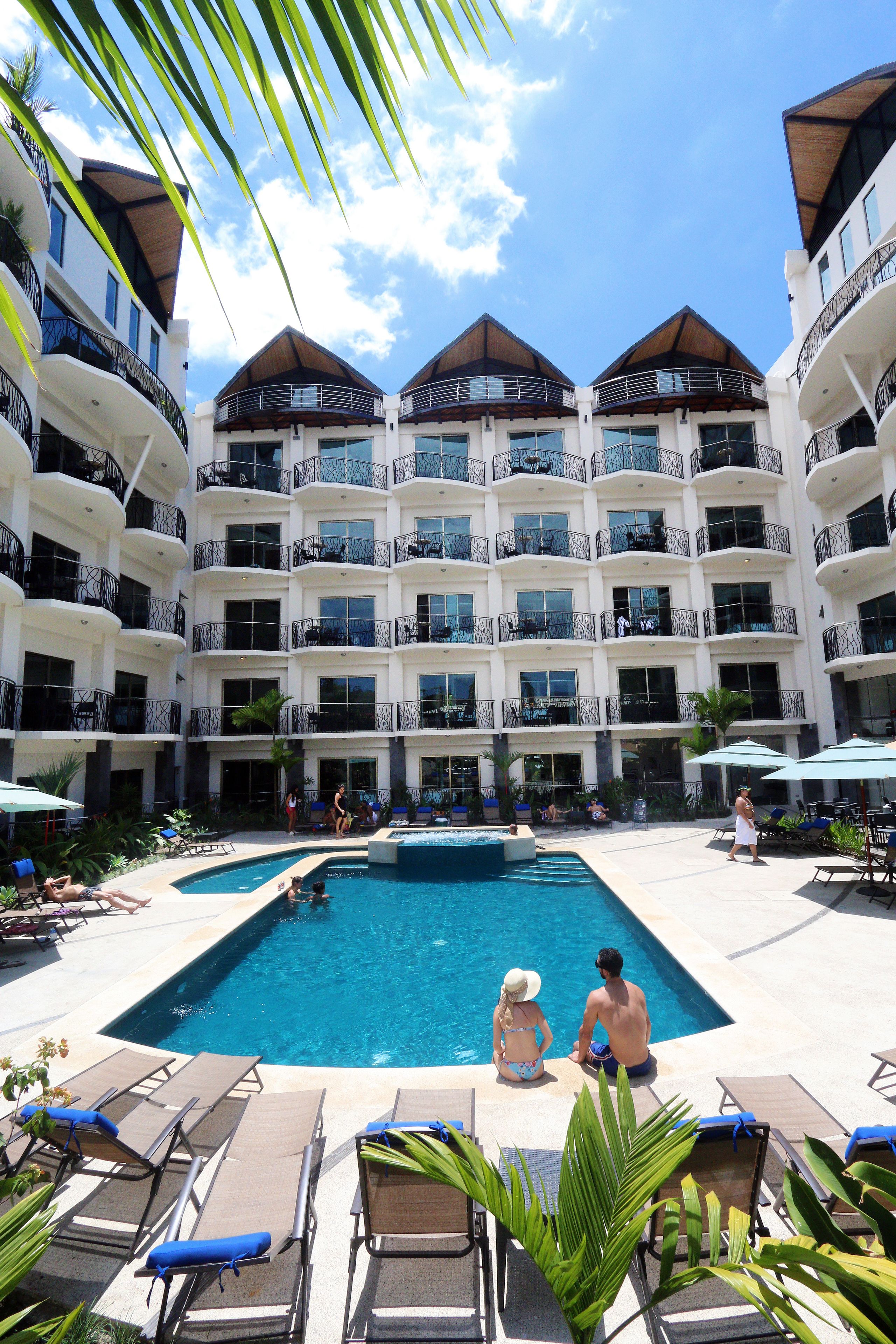 A hotel with multiple balconies, a swimming pool, and lounge chairs.