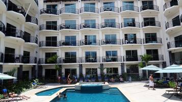 Un hotel con varios balcones, piscina y sillones de descanso.