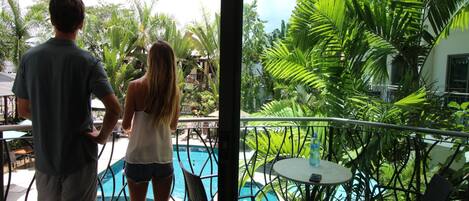 Un hombre y una mujer están junto a una piscina, con vistas a un jardín exuberante y un edificio al fondo.