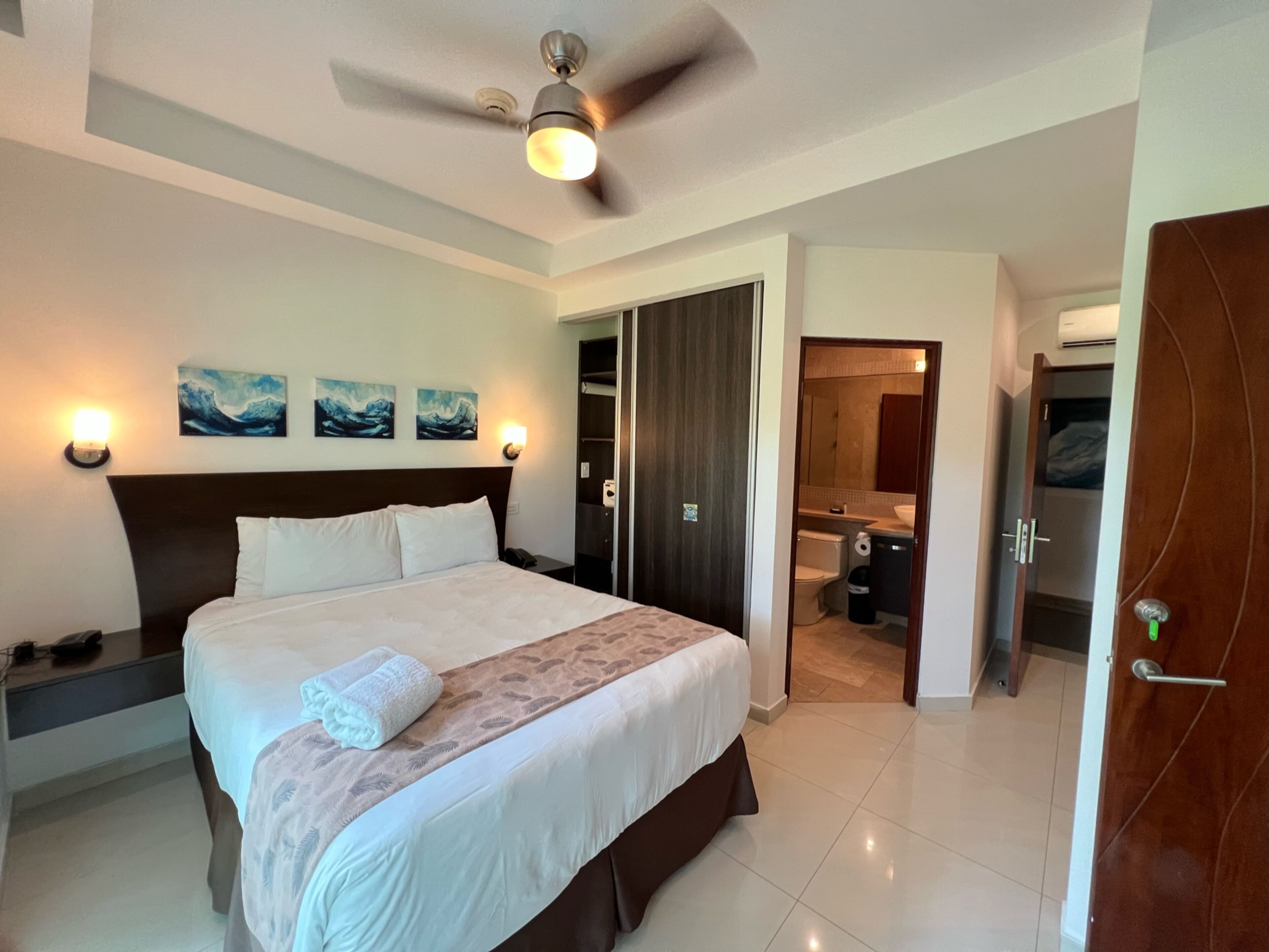 Una habitación de hotel con una cama grande, un ventilador de techo y obras de arte en la pared.