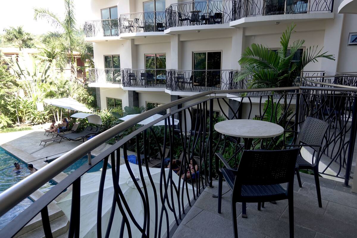 A balcony with a pool, outdoor seating, and a view of the surrounding greenery.