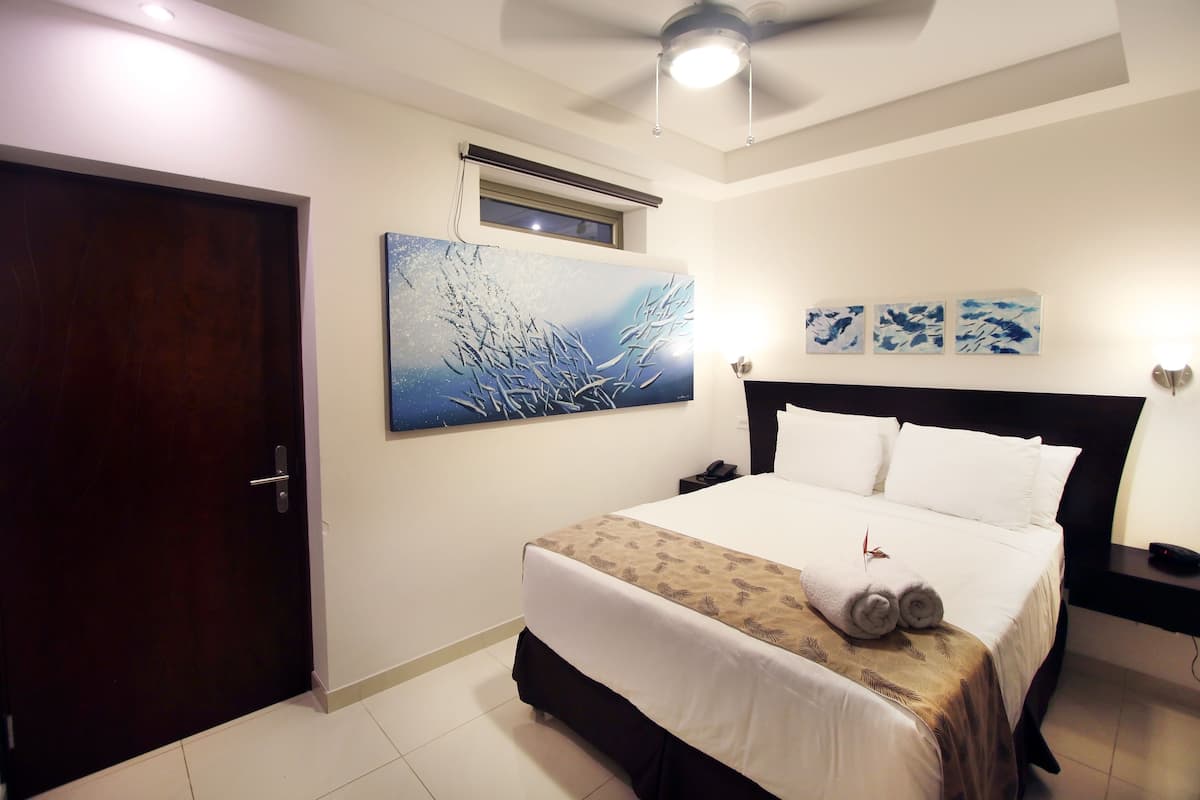 A hotel room with a bed, a ceiling fan, a window, and artwork on the wall.