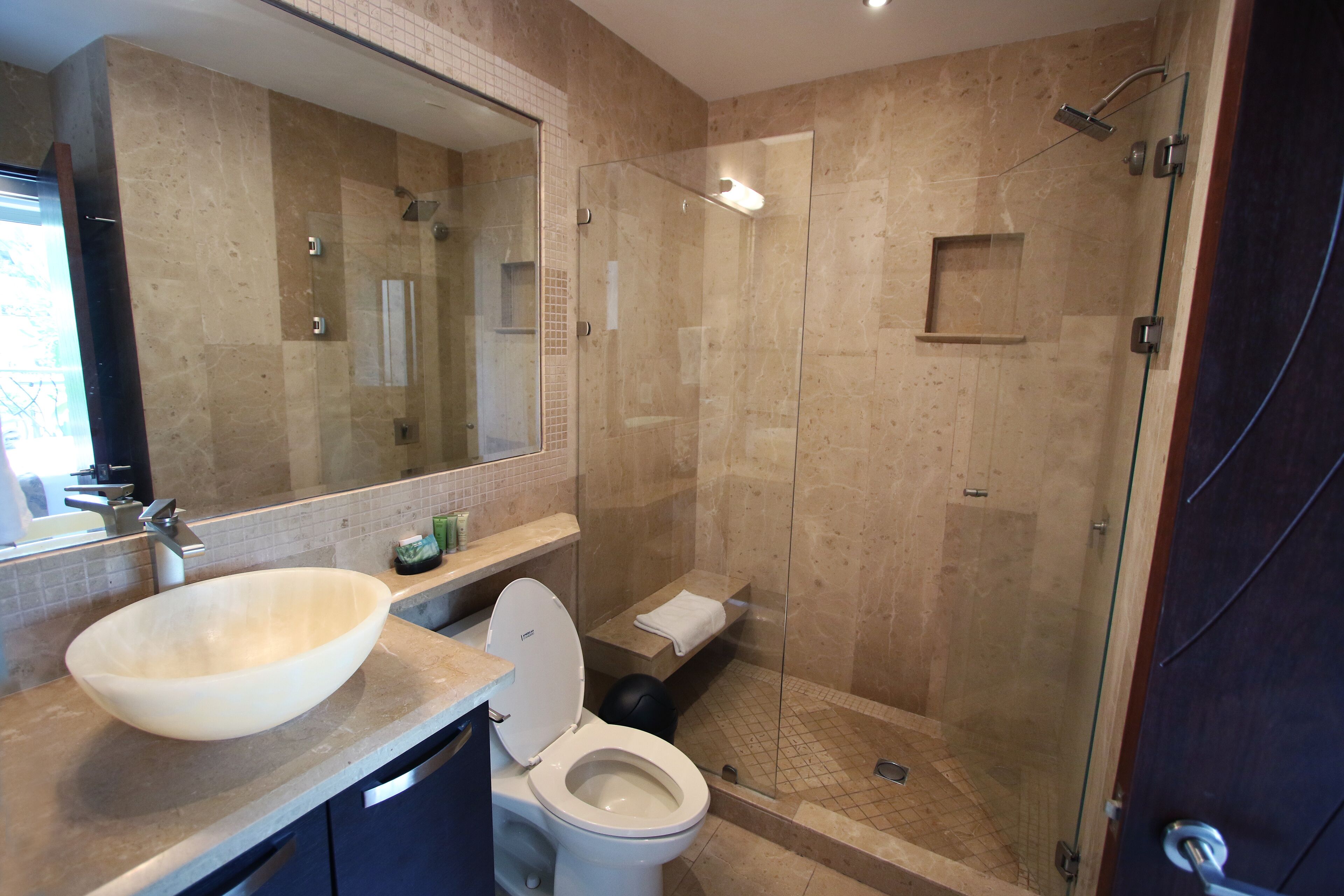 A modern bathroom with a large mirror, a beige sink, a toilet, and a glass-enclosed shower area.