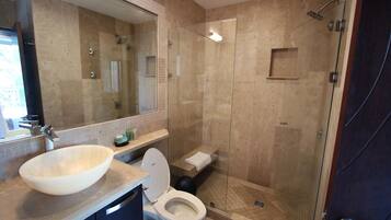 A modern bathroom with a large mirror, a beige sink, a toilet, and a glass-enclosed shower area.