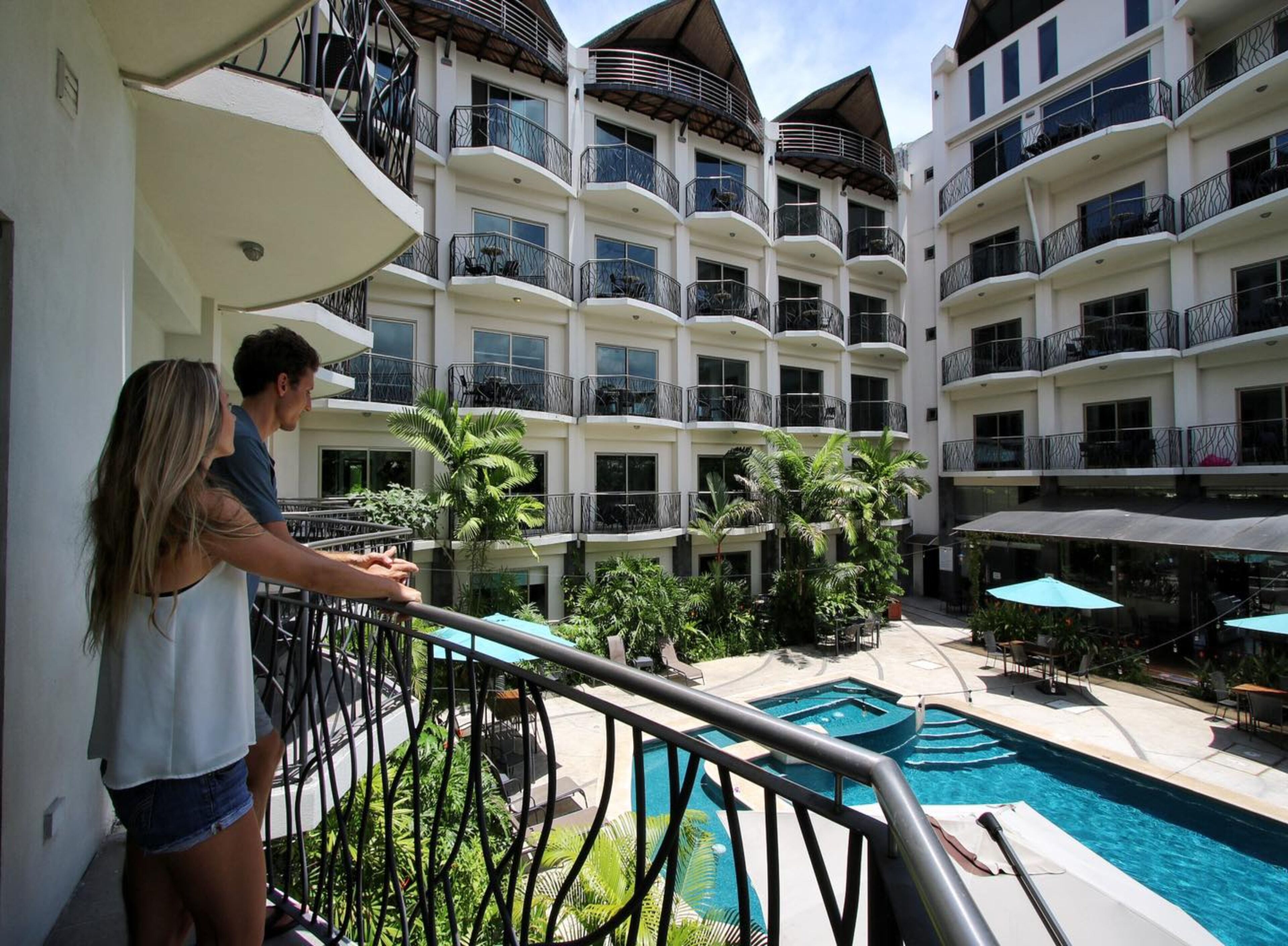 Un hotel de varios pisos con balcones, piscina y zonas de estar al aire libre.