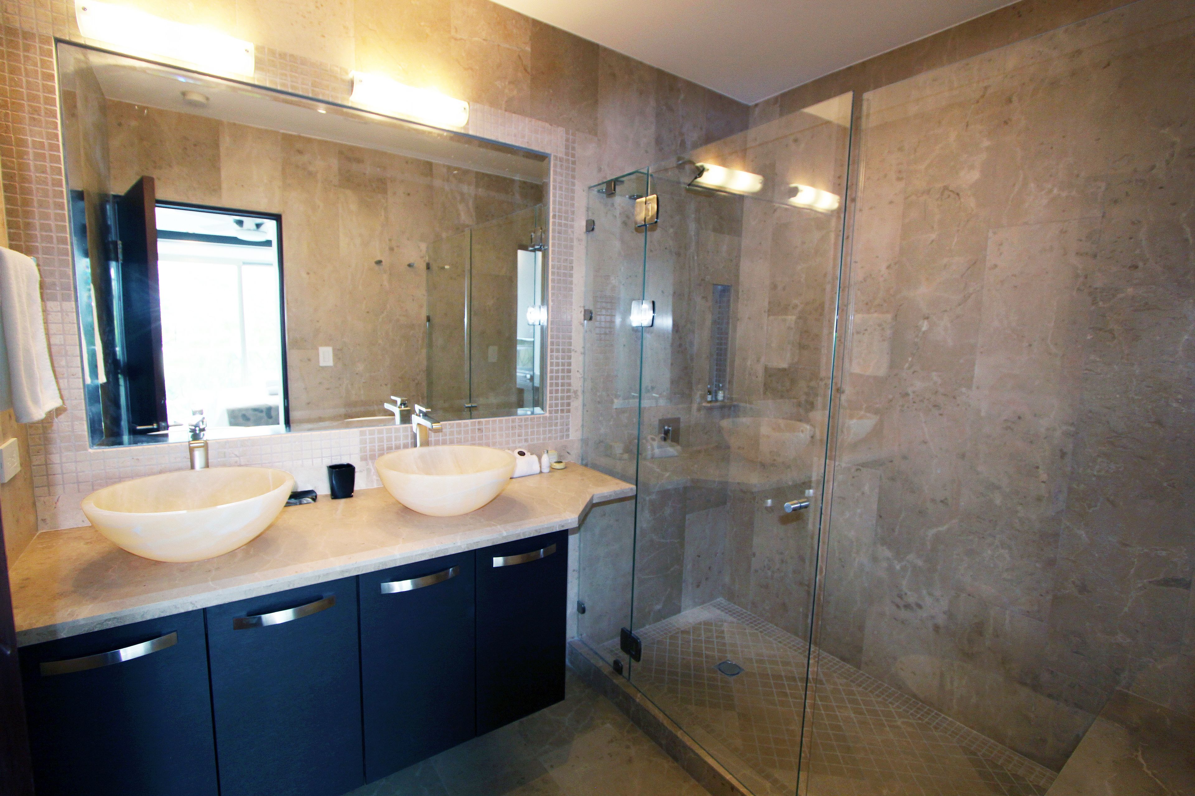 Un baño moderno con dos lavamanos grandes, una cabina de ducha de vidrio y un espejo amplio.