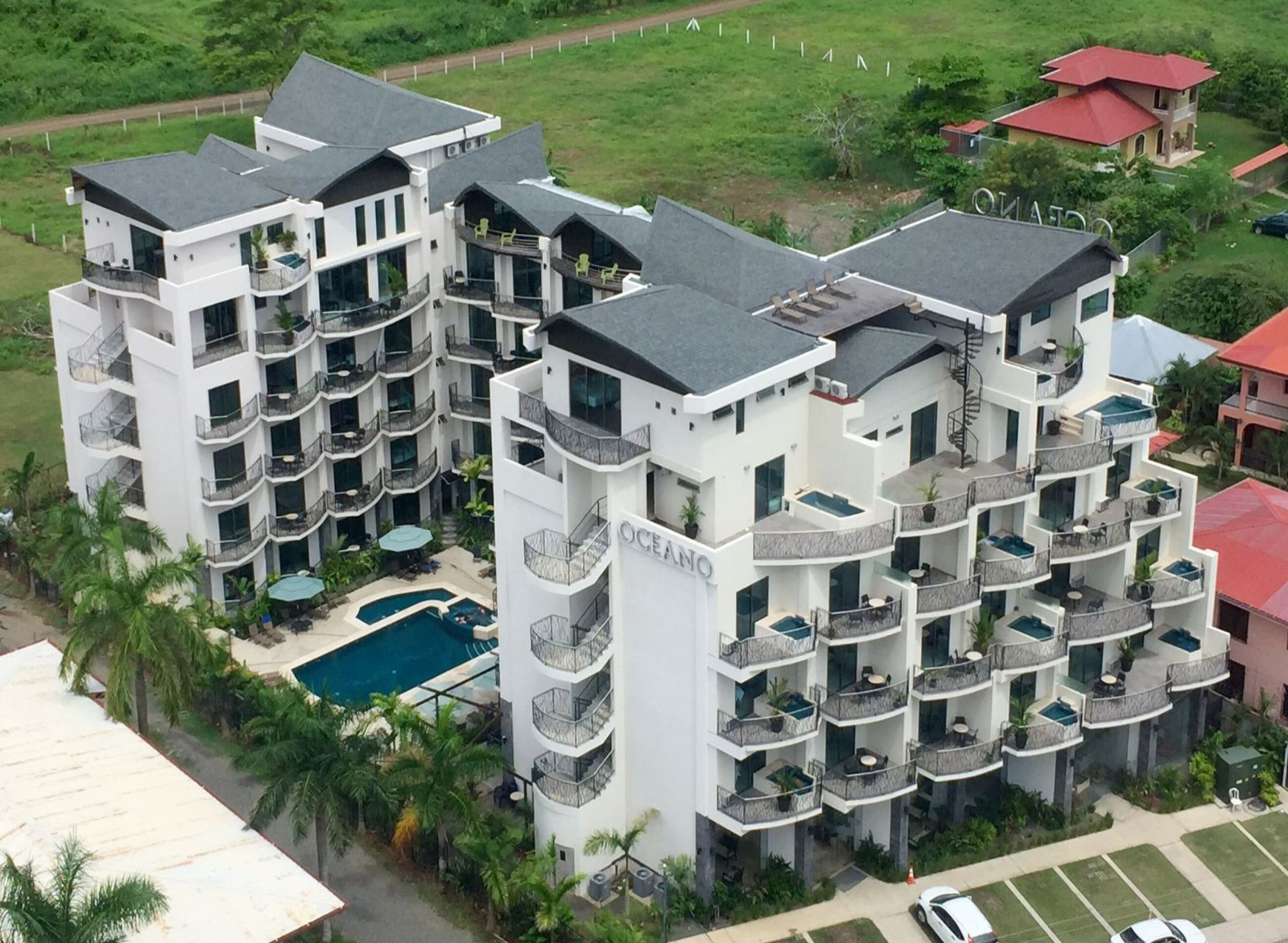 A multi-story hotel with balconies, a swimming pool, and a lush green environment.