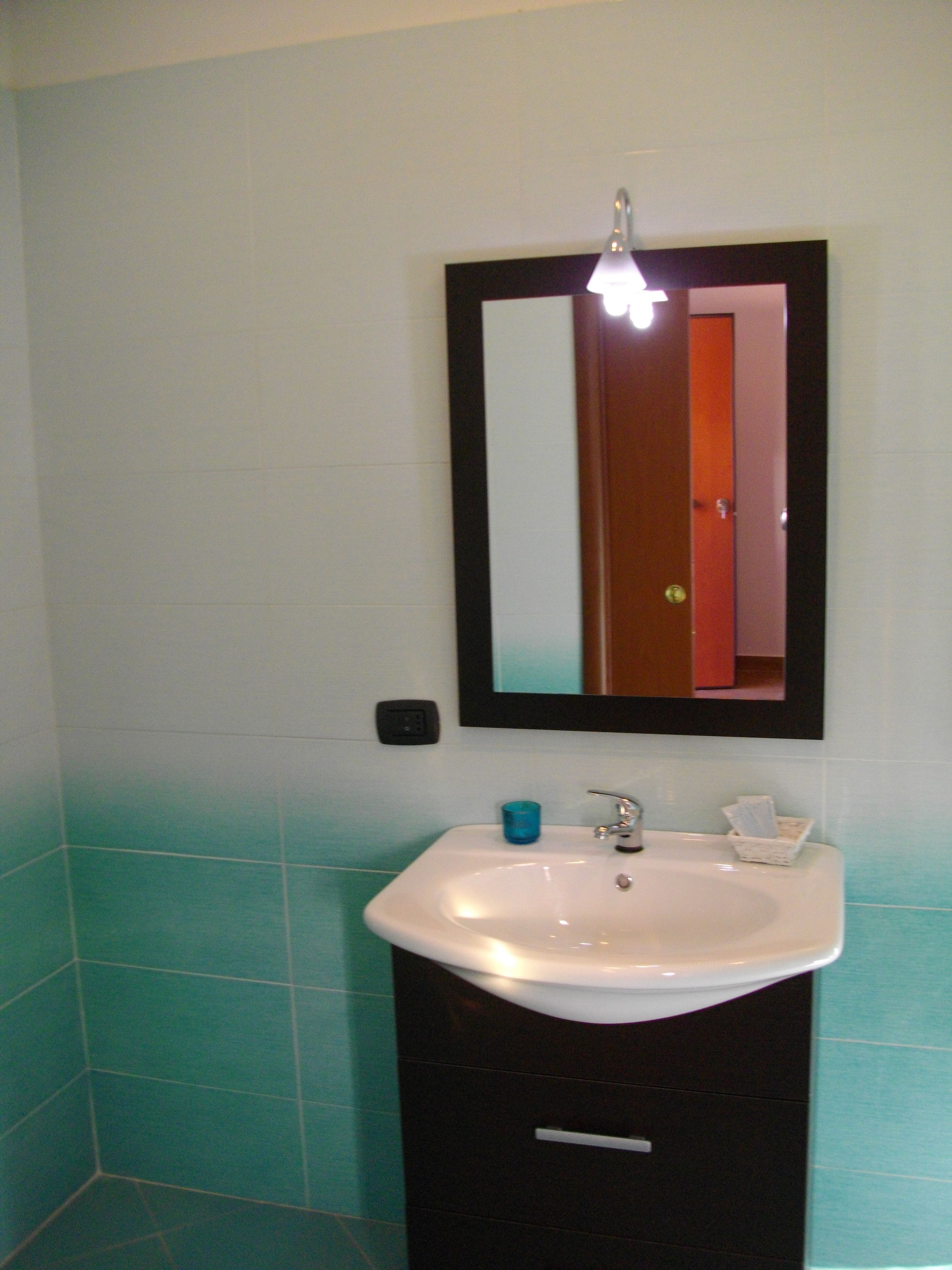 Une salle de bain avec un lavabo blanc, un miroir et une porte donnant sur une autre pièce.