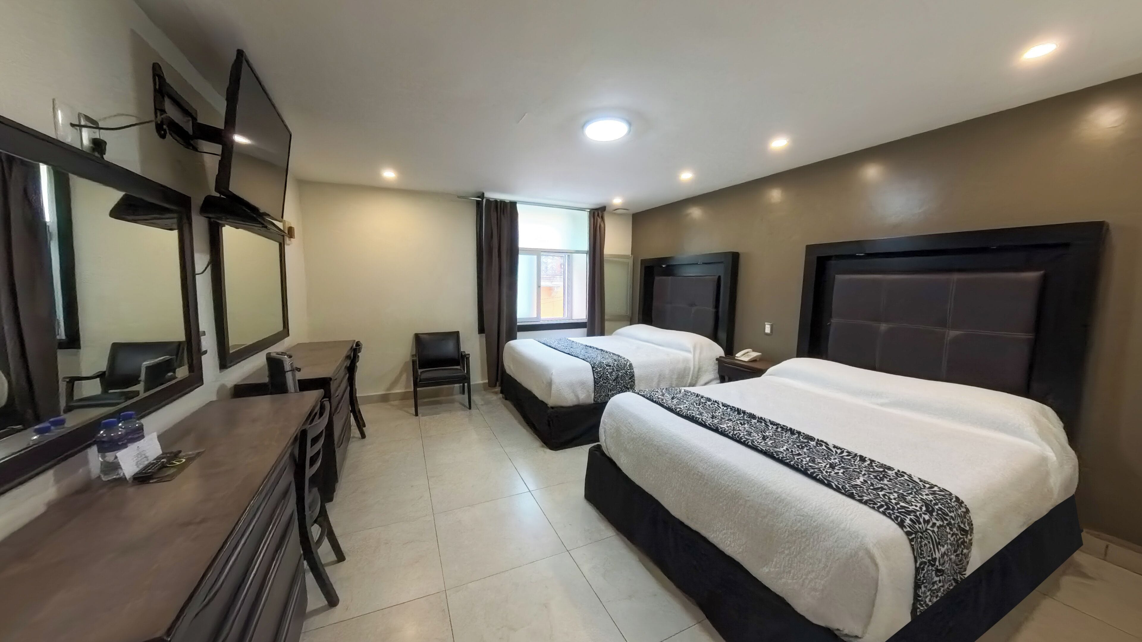 Habitación de hotel con dos camas, un escritorio, una silla, televisión y ventana con cortinas.