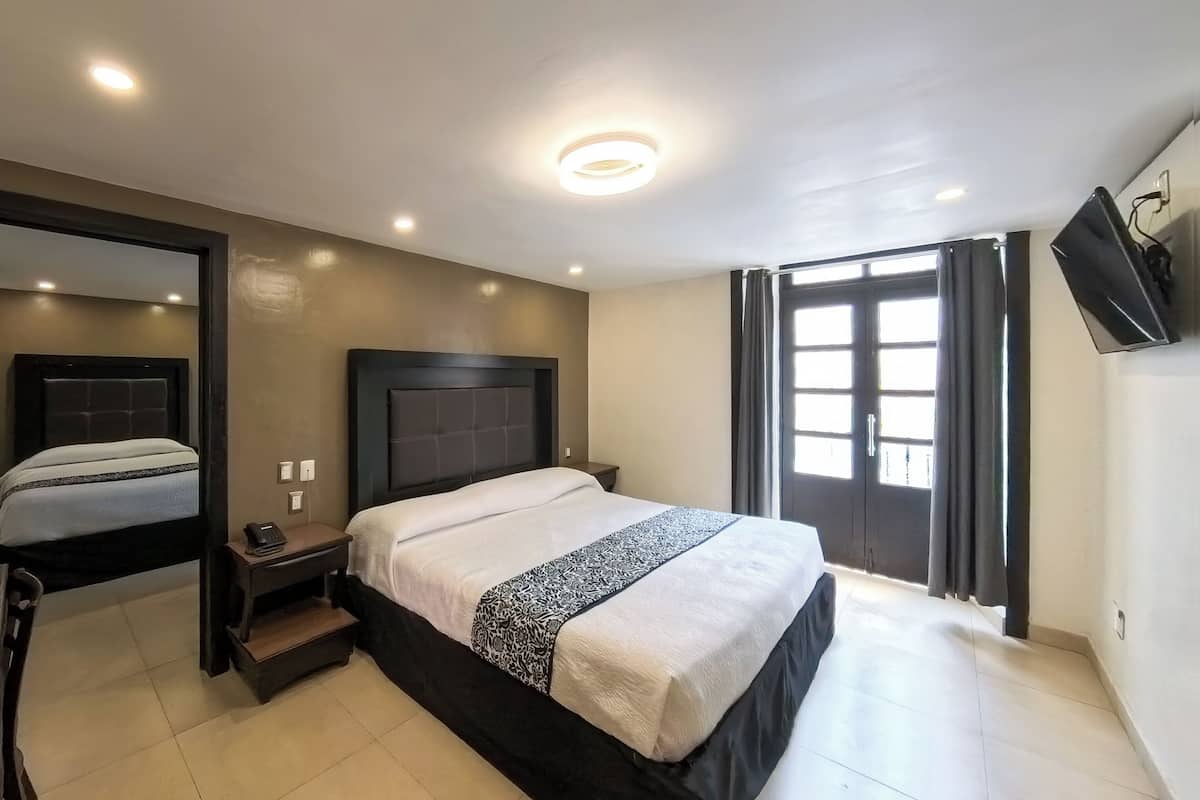 A modern hotel room with a large bed, a desk, a chair, a nightstand, and a TV.