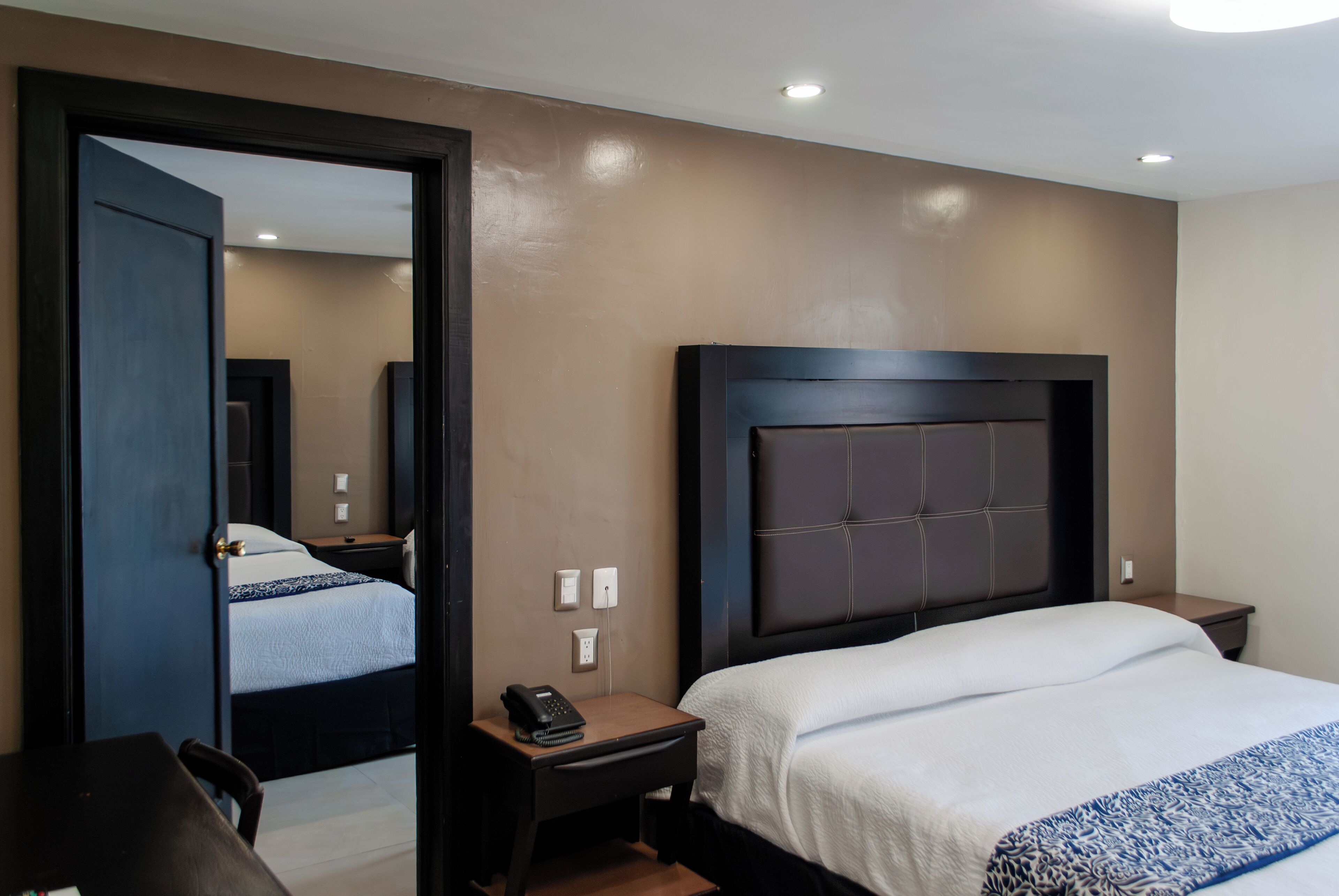Habitación de hotel con una cama grande, una mesita de noche con teléfono, una lámpara y un espejo.