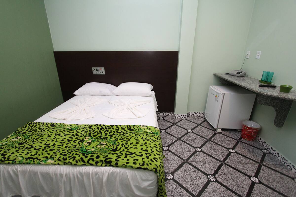 Habitació d'hotel amb un llit, un mini frigorífic, una taula de nit amb un telèfon i gots, i un sòl amb un disseny.