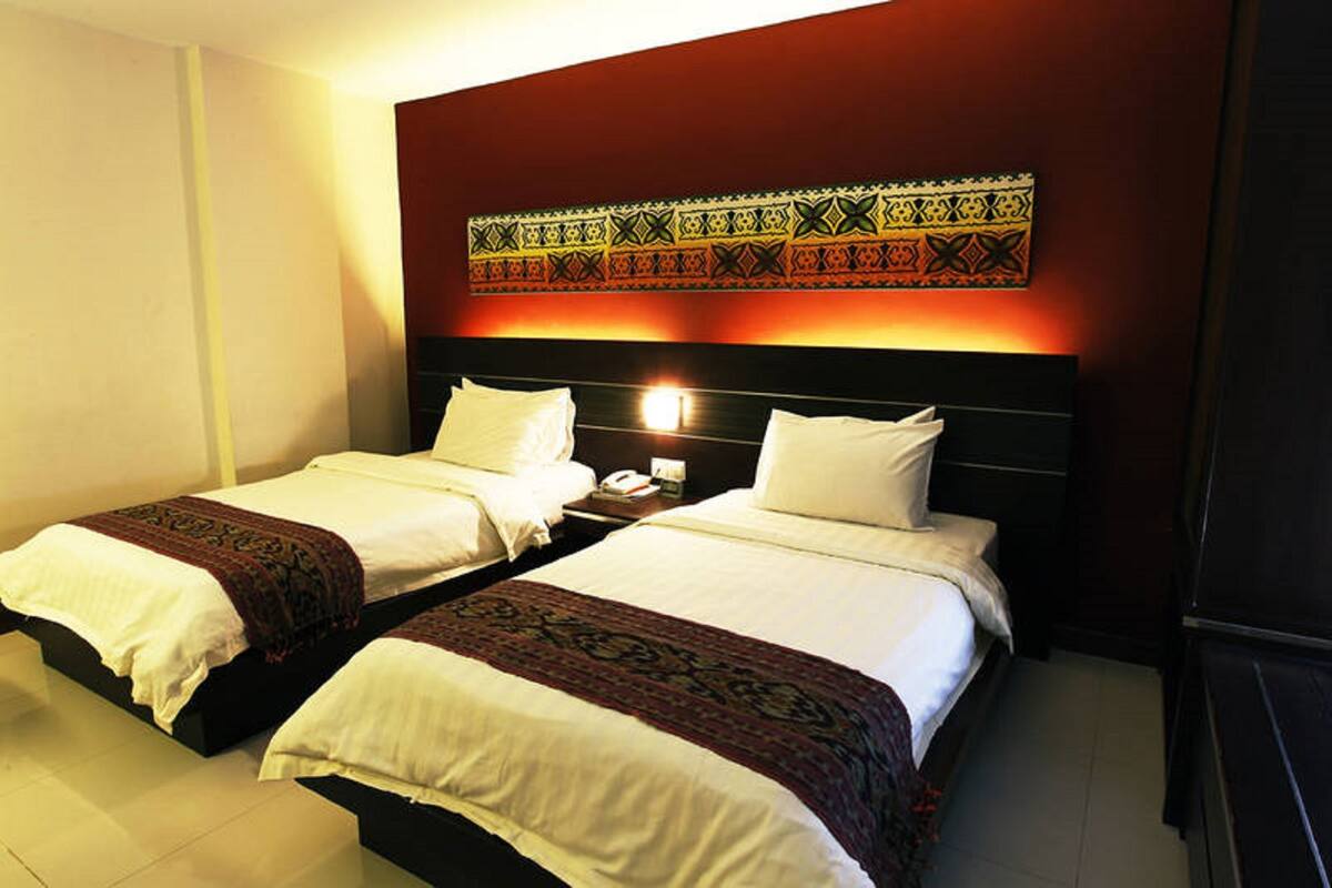 A hotel room with two beds, a headboard with a decorative panel, and a bedside table with a lamp.