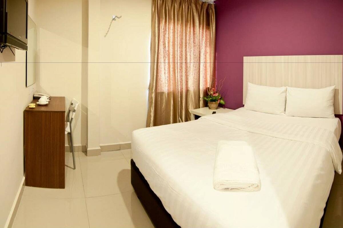 A hotel room with a bed, a bedside table, a shower, and a bathroom mirror.