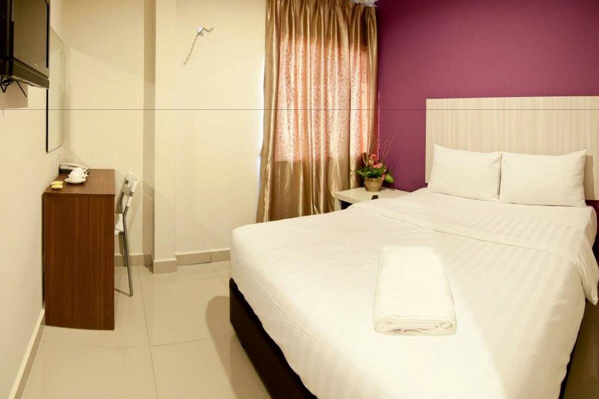 A hotel room with a bed, a bedside table, a nightstand, a shower, and a bathroom.
