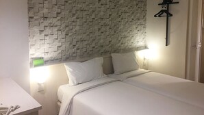 A bedroom with a textured wall, a bed with white bedding, a bedside table with a lamp, and a coat rack with a teddy bear. - 101 Hotel Bangi (Bandar Baru Bangi)