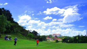A golf course with players and a golf cart, surrounded by greenery and a building with a red roof in the background. - 101 Hotel Bangi (Bandar Baru Bangi)