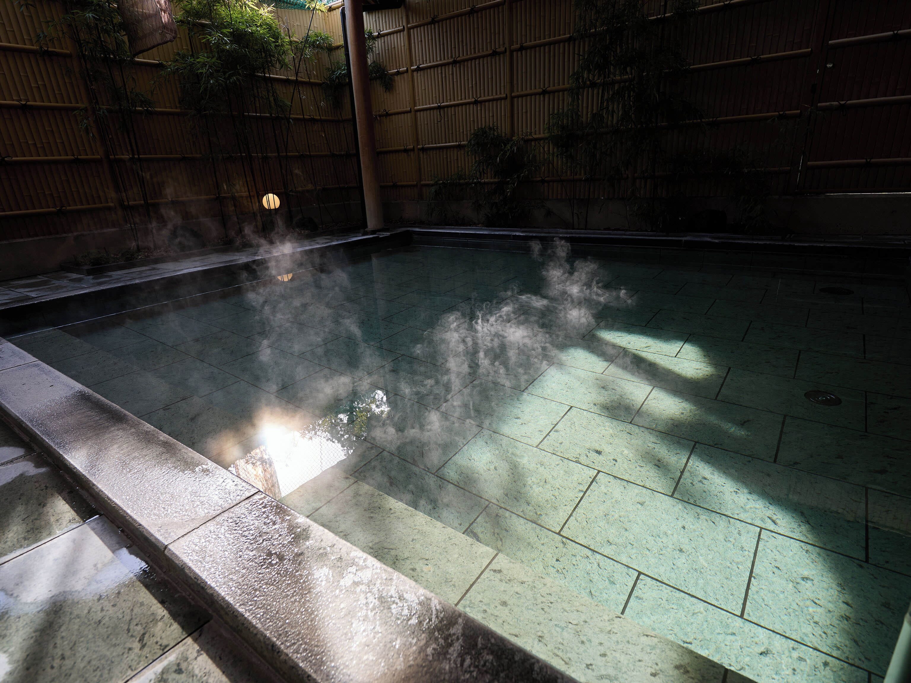 Une piscine avec un sol carrelé et une clôture en bambou en arrière-plan.