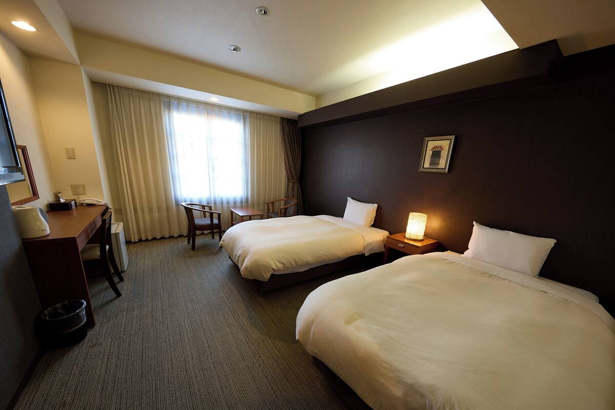 A hotel room with two beds, a desk, and a chair.