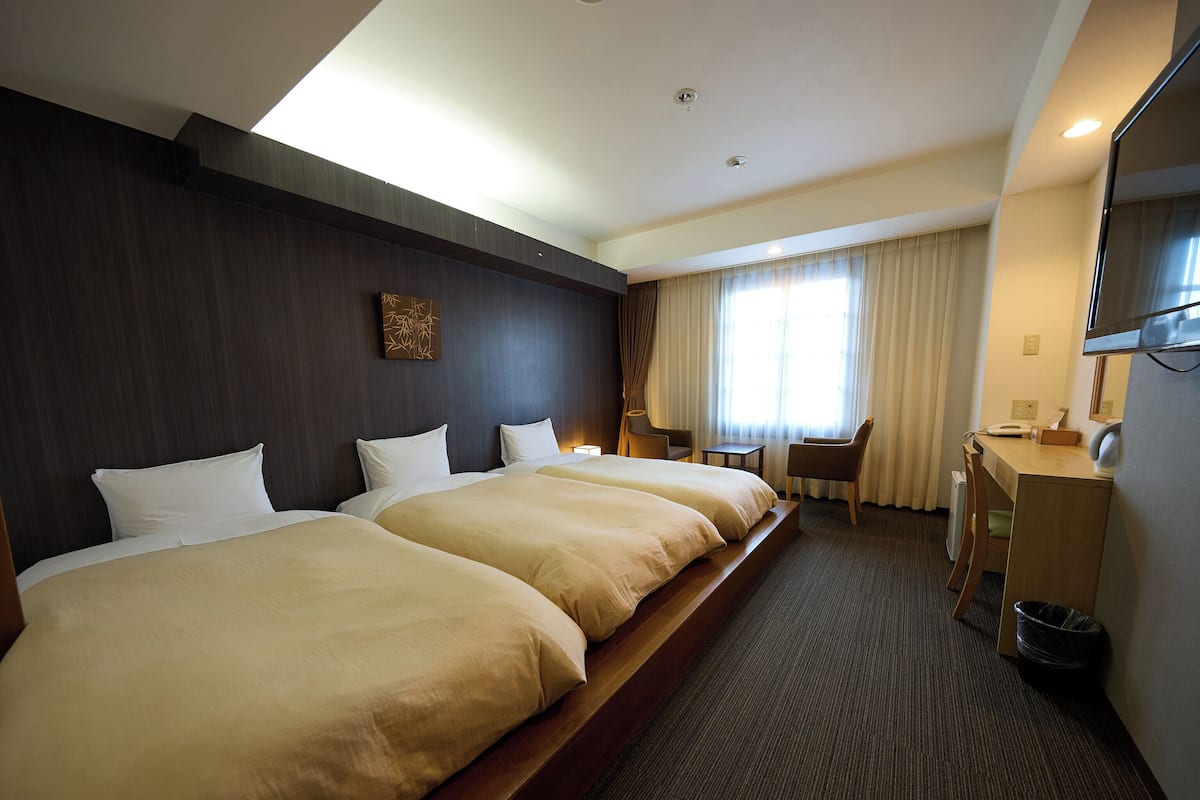 A hotel room with two beds, a desk, a chair, a TV, and a window with curtains.