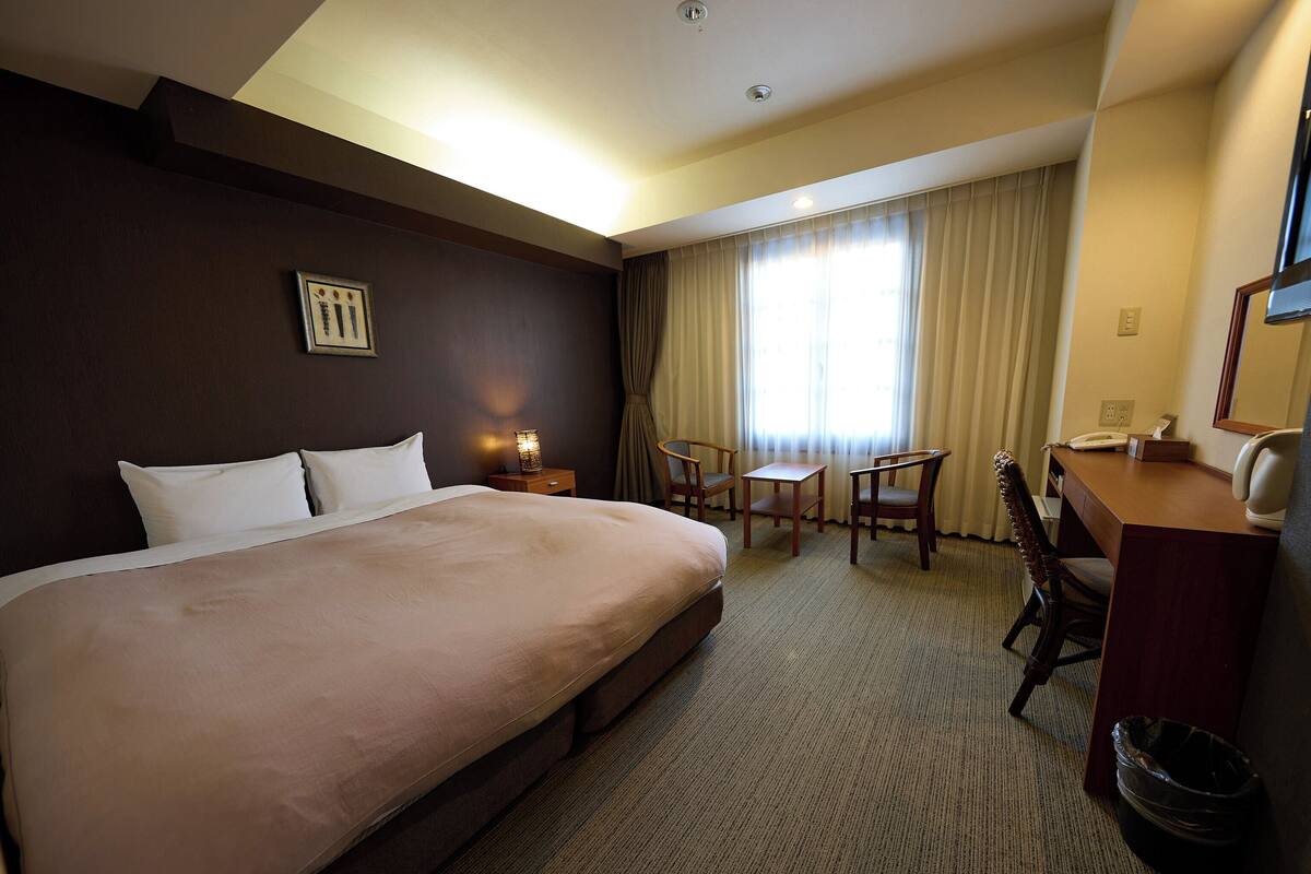 A hotel room with a large bed, a desk with a telephone, and a chair.