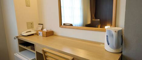 A hotel room with a wooden desk, a chair, a telephone, a tissue box, a kettle, and a mirror.