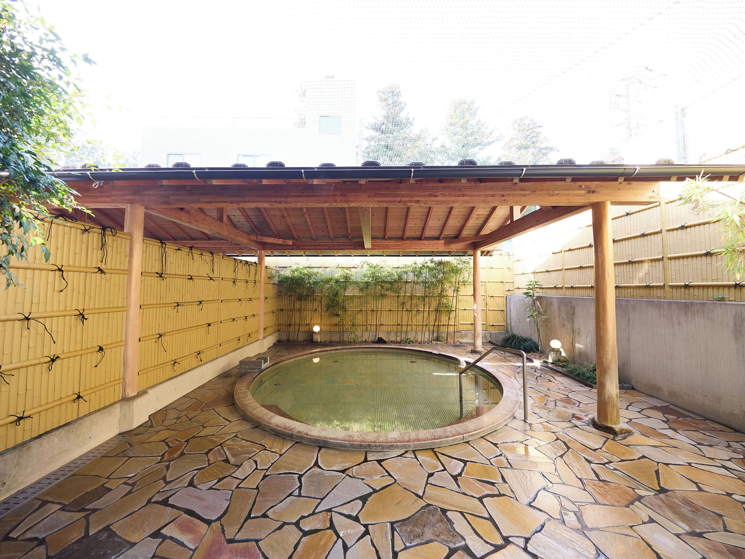 Una piscina exterior cubierta con suelo de piedra y paredes de bambú.
