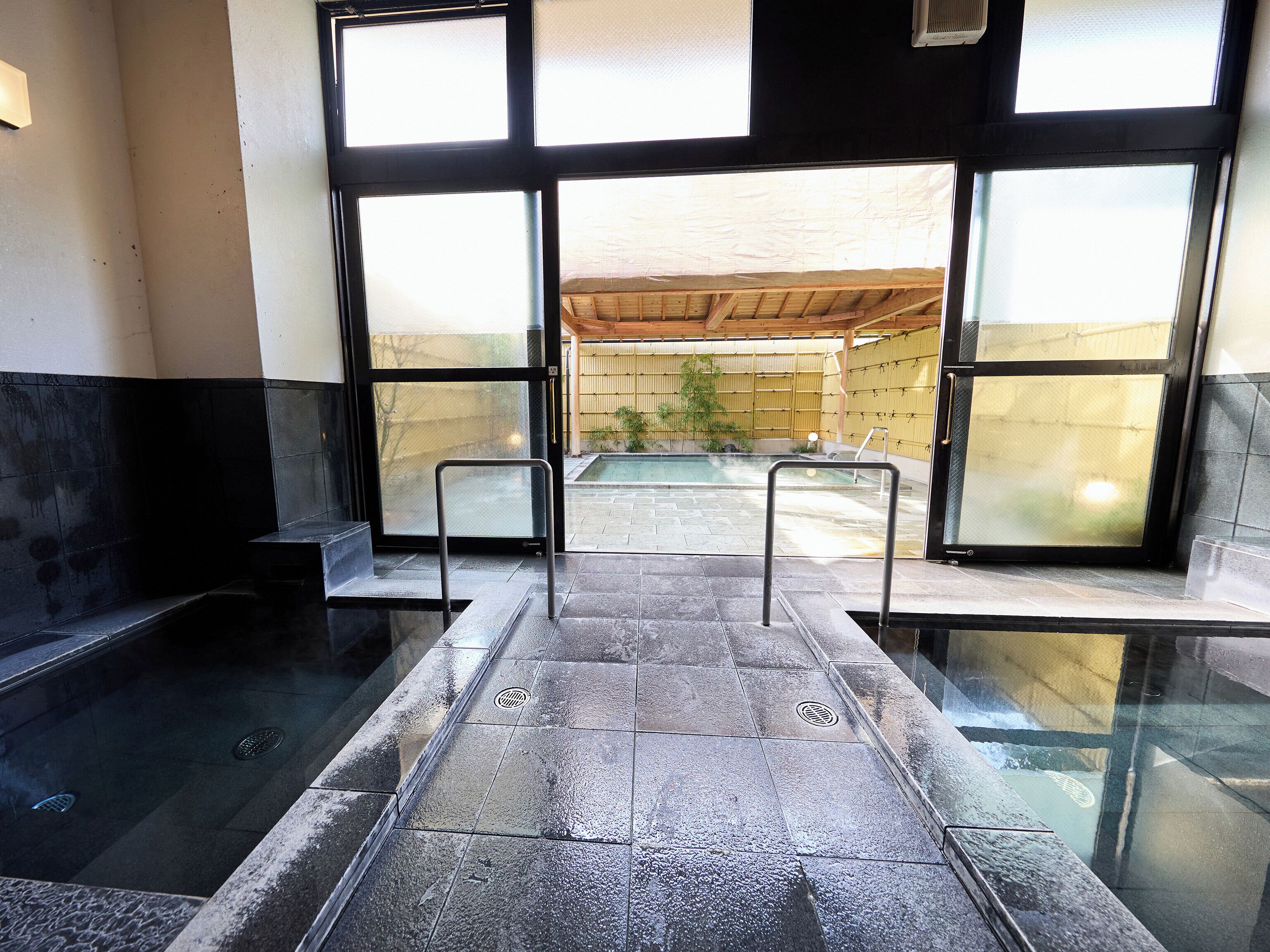A stone-tiled indoor pool area with metal railings and a view of an outdoor pool through large windows.