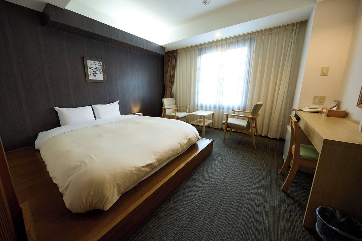 A hotel room with a large bed, a desk, a chair, and a small table.