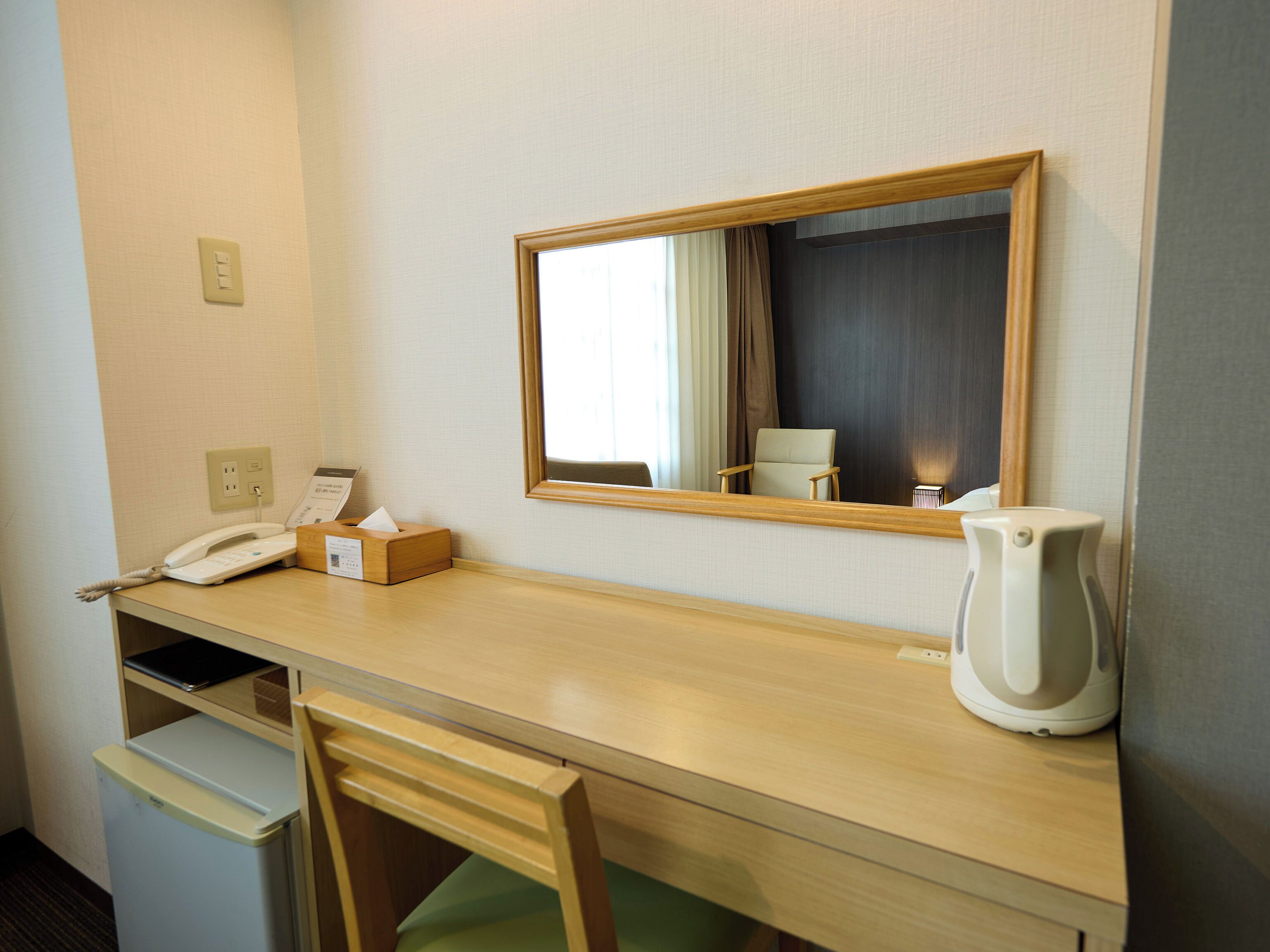 Een hotelkamer met een houten bureau, een telefoon, een zakdoosjesbakje, een waterkoker en een stoel.