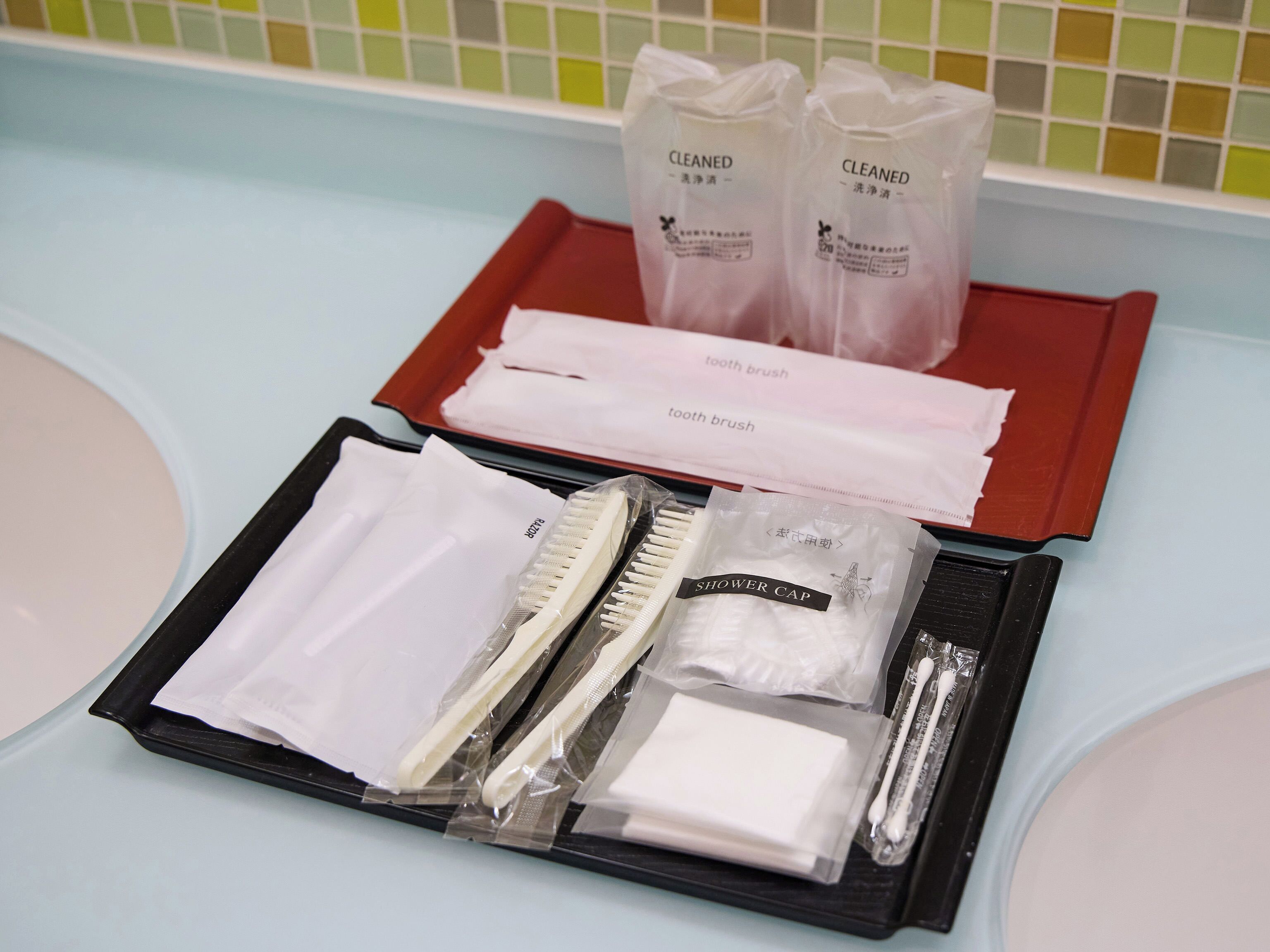 A bathroom with a light blue countertop, a red tray, and a set of toiletries including a toothbrush, toothpaste, and a shower cap.