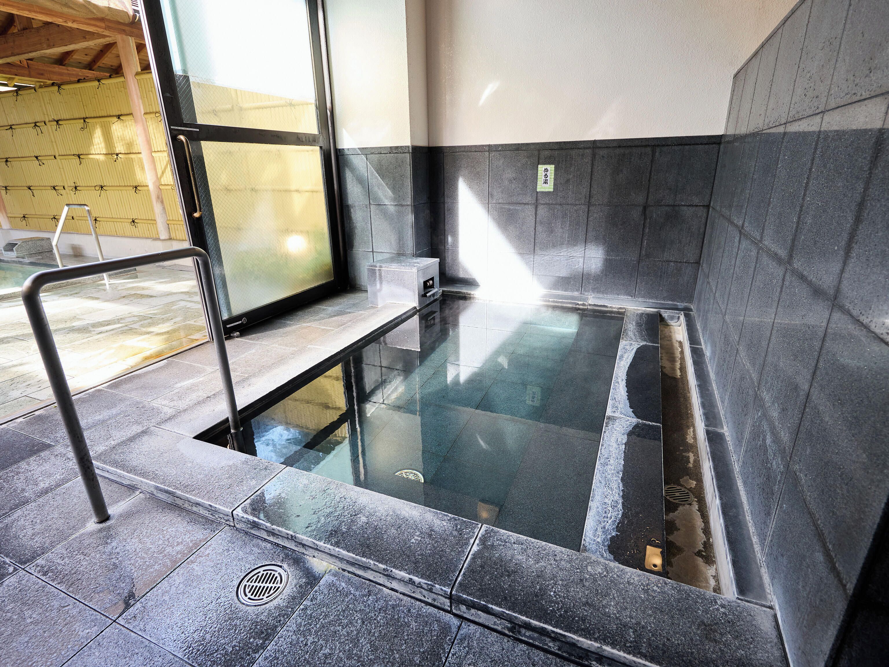 A modern indoor hot tub area with a glass enclosure, metal railings, and tiled walls.