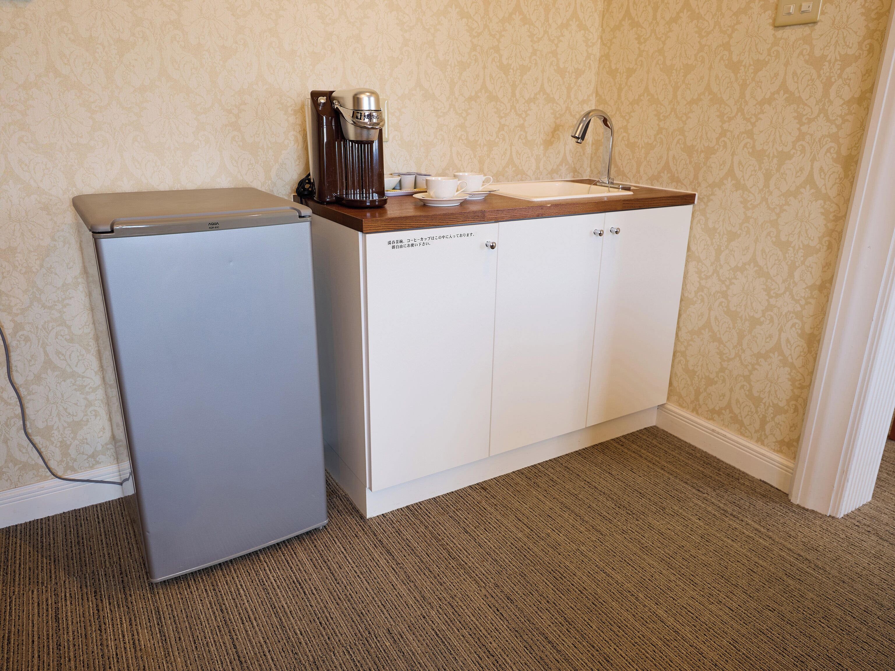 A compact kitchenette with a refrigerator, a coffee maker, and a sink.