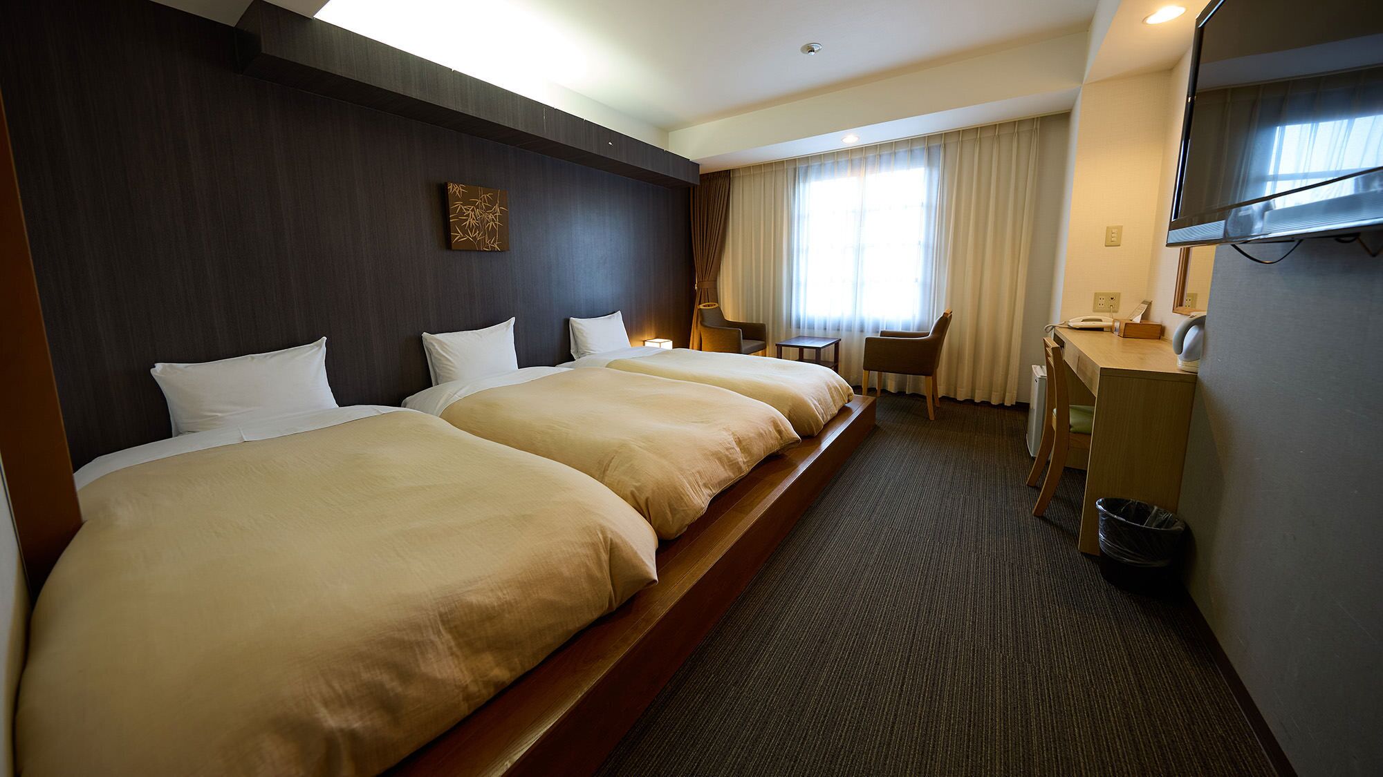 A hotel room with two beds, a desk, a chair, a TV, and a window with curtains.