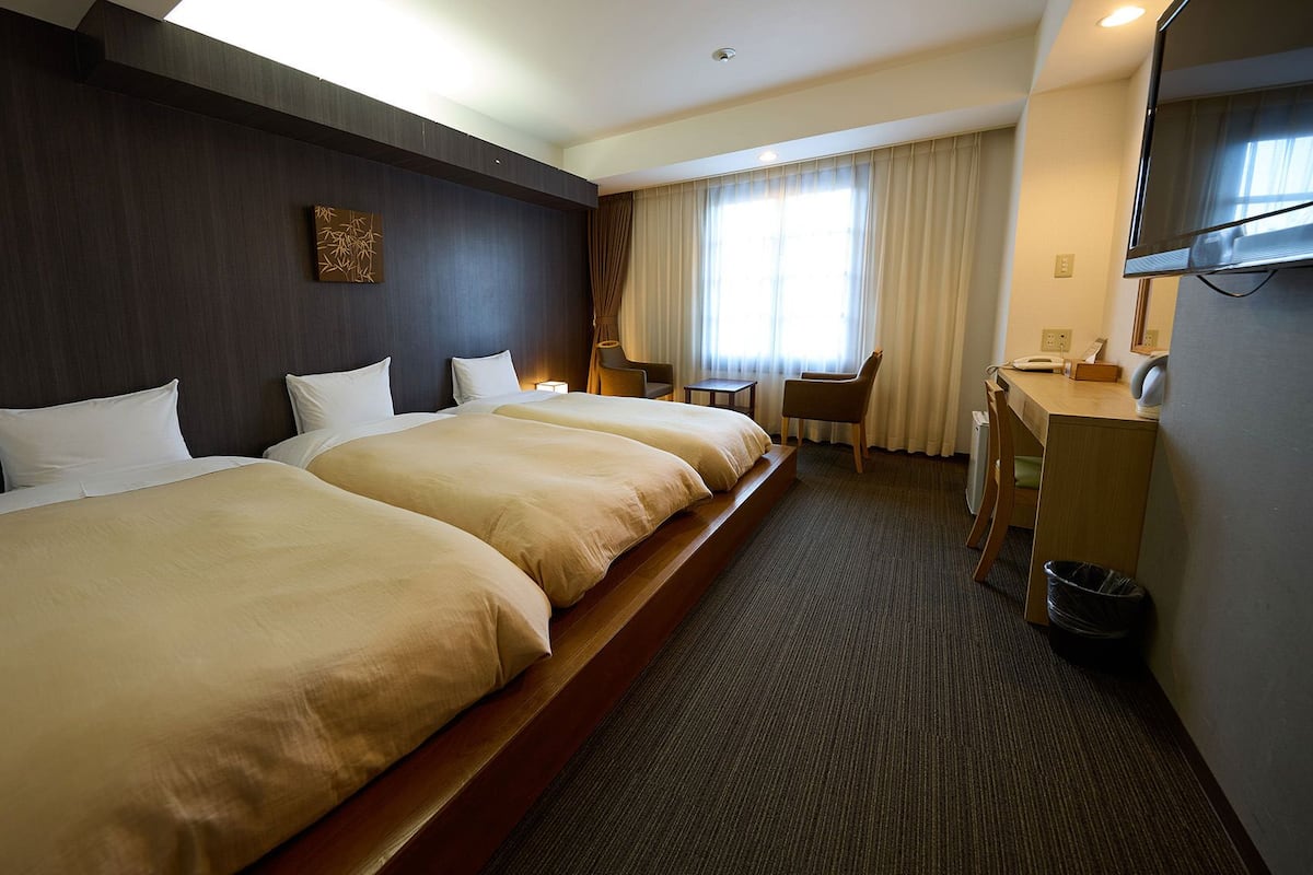 A hotel room with two beds, a desk, a chair, a TV, and a window with curtains.