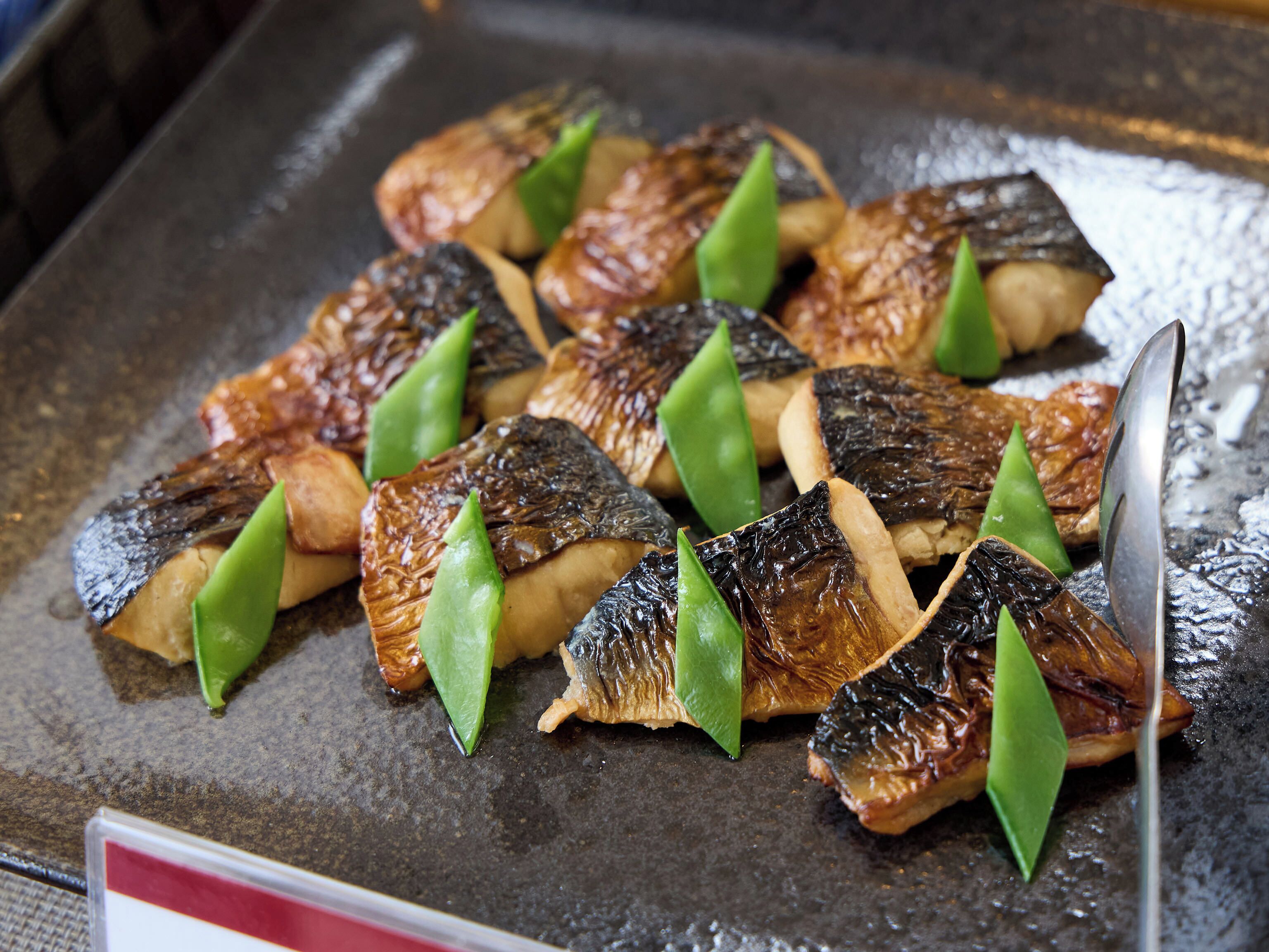 A tray of grilled fish and green vegetables on a metal surface.
