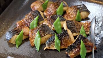 A tray of grilled fish and green vegetables on a metal surface.