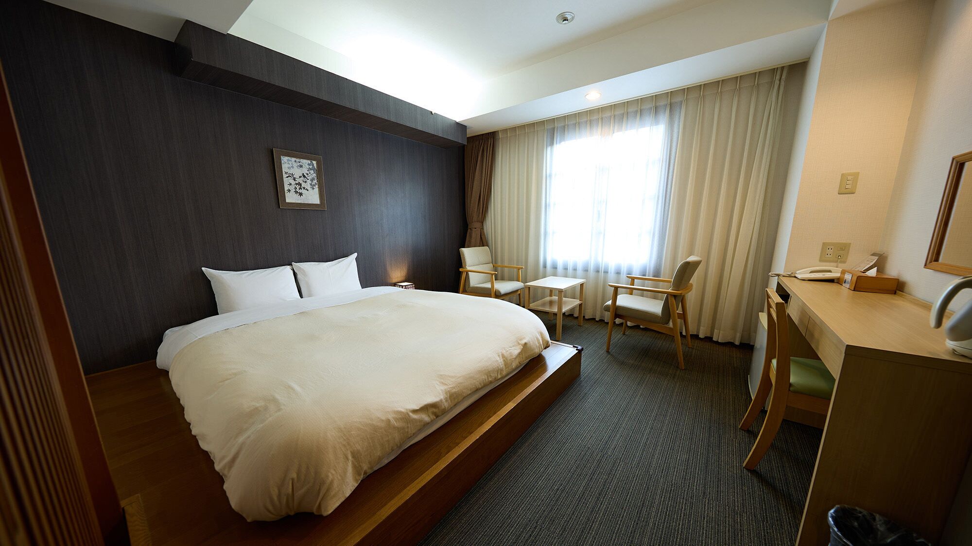 A hotel room with a large bed, a desk with a telephone, a chair, and a small table.