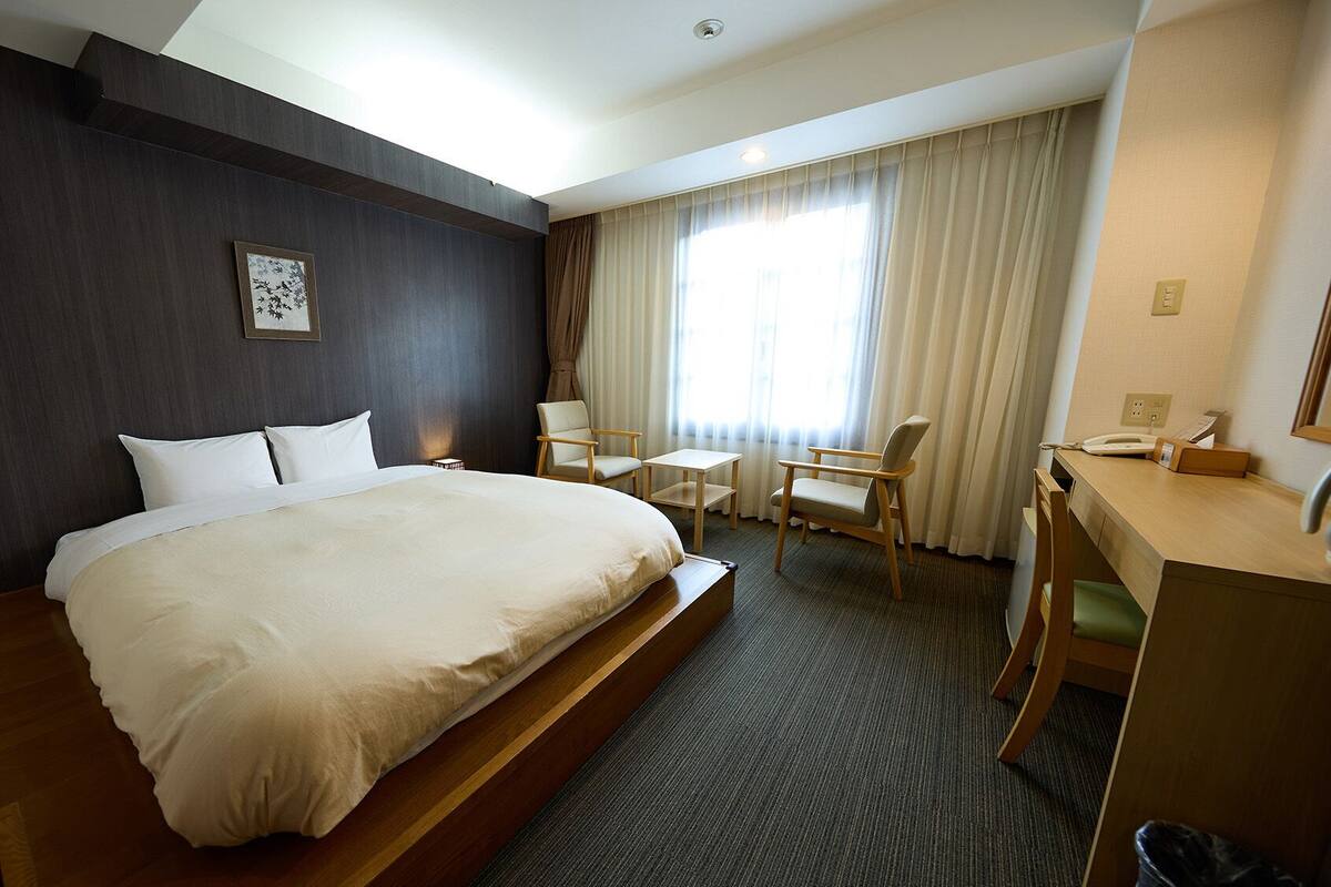 A hotel room with a large bed, a desk with a telephone, a chair, and a small table.